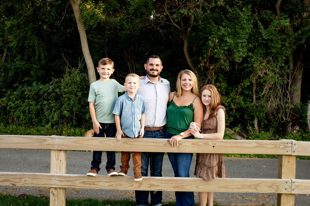 Family poses together on wooden fence during outdoor photo session.