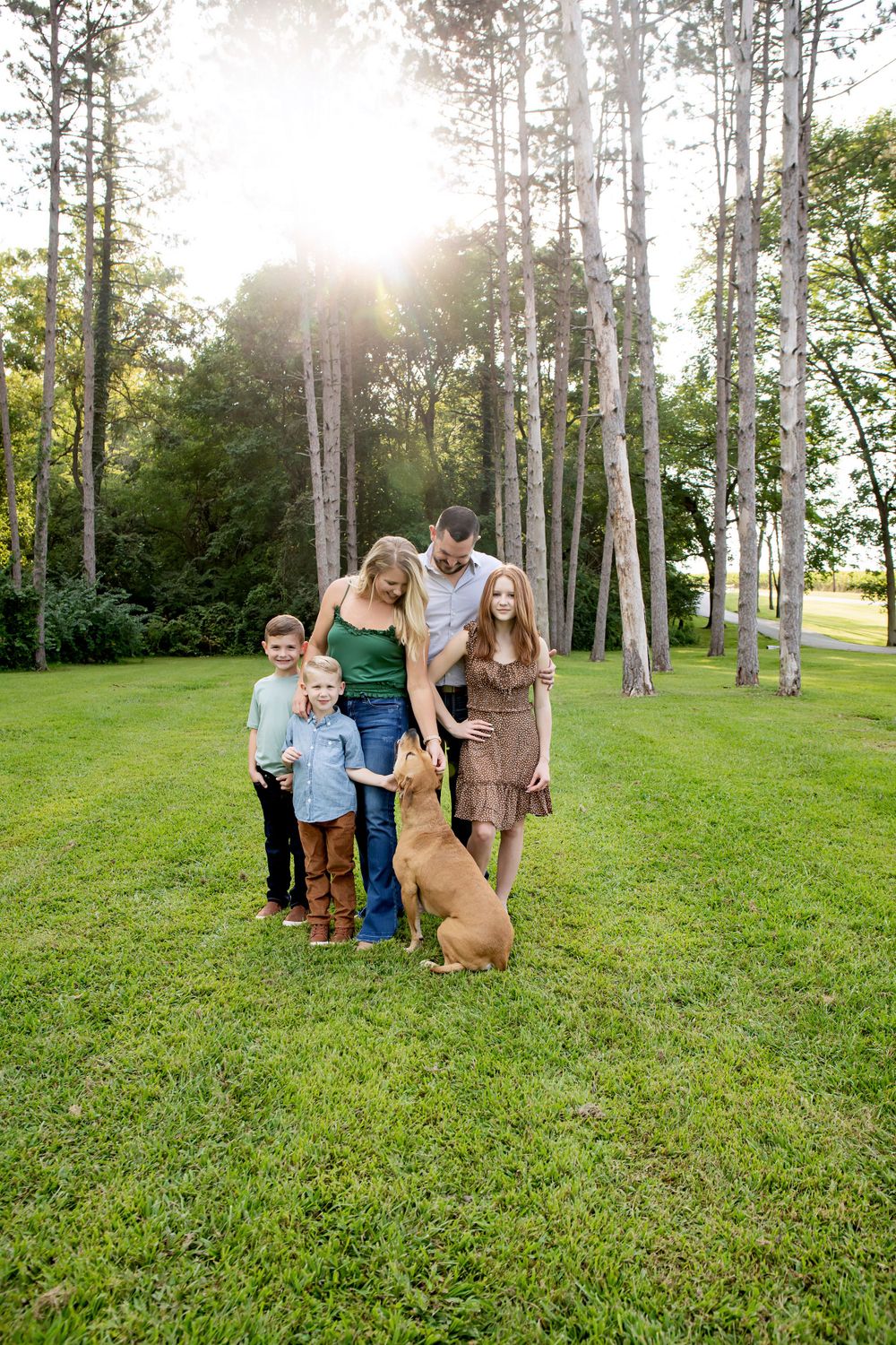 Family group poses with their golden retriever in a sunny birch grove.