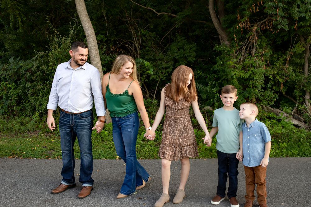 Family holding hands while walking together on a tree-lined path.