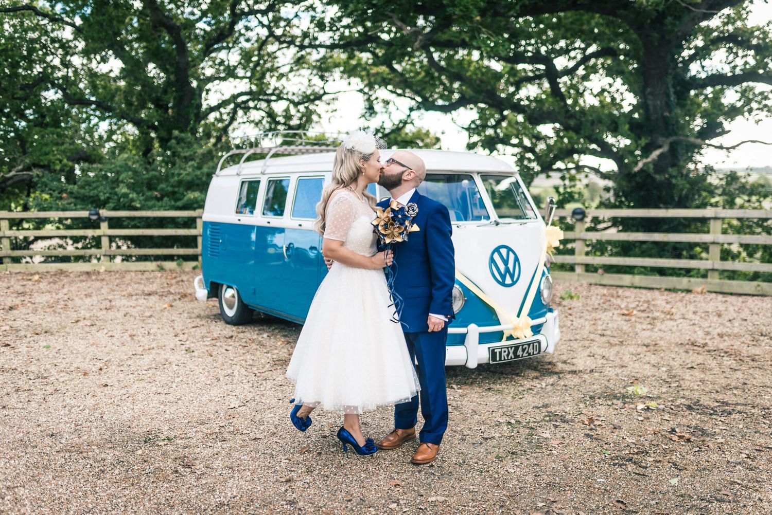 A couple poses in front of a classic blue and white VW camper van.