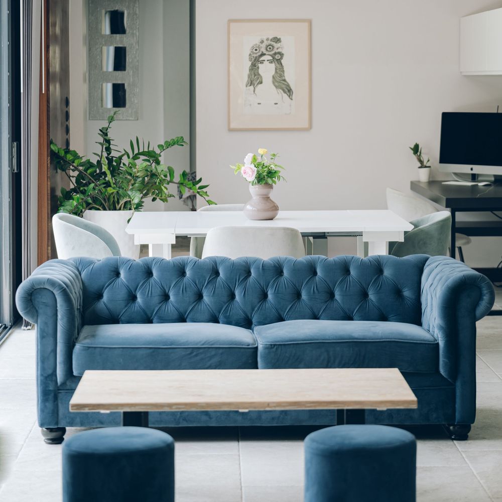 Modern living room with blue tufted Chesterfield sofa, round coffee table and botanical wall art.