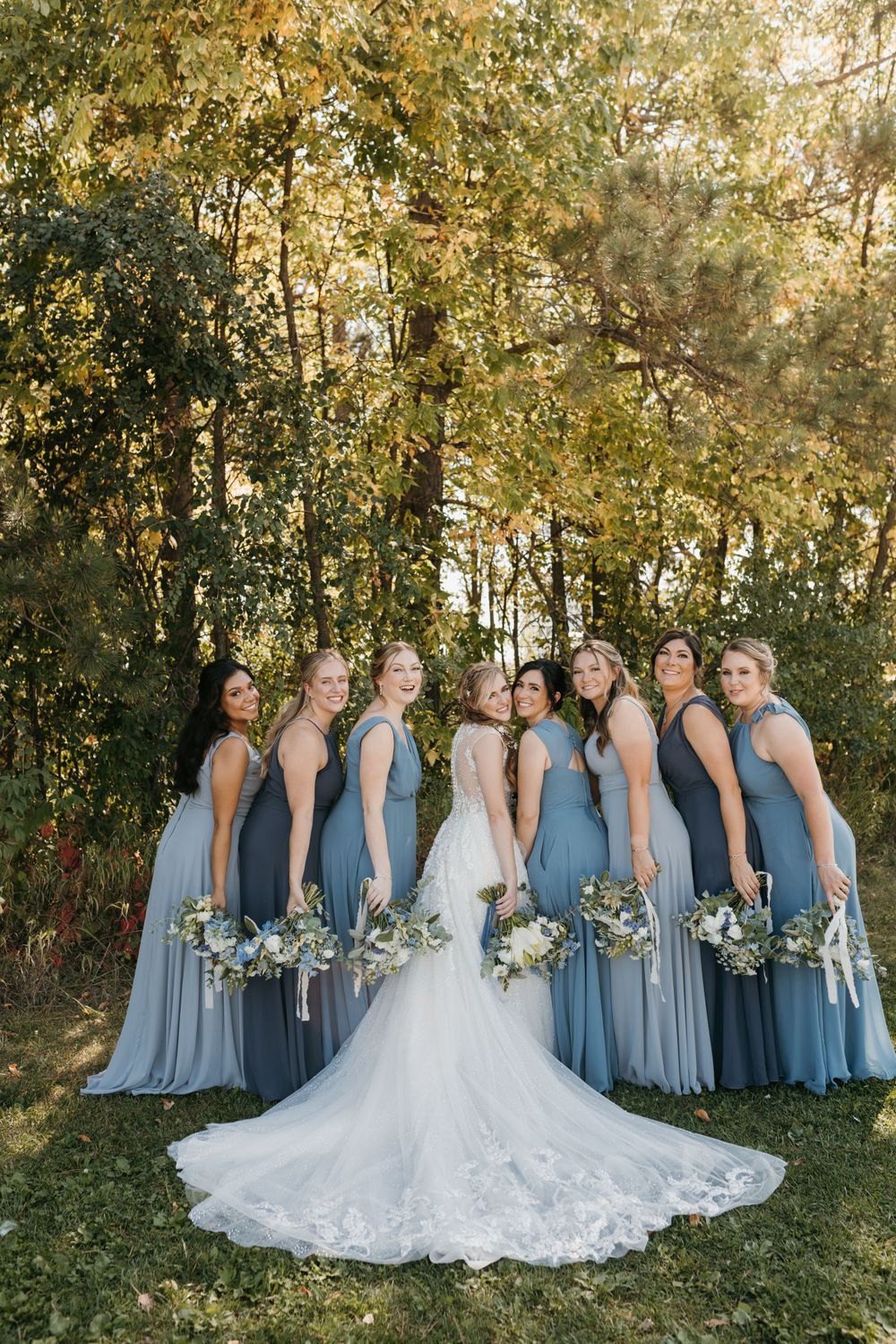 Bride with lace train surrounded by bridesmaids in blue gowns holding bouquets.