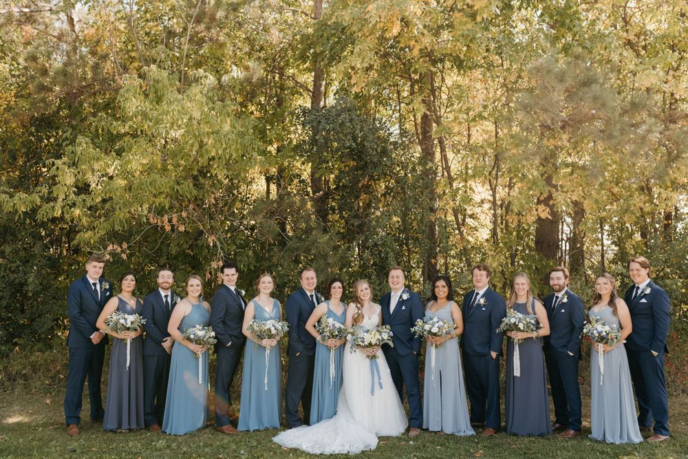 Large wedding party posing together in autumn setting with blue and navy attire.