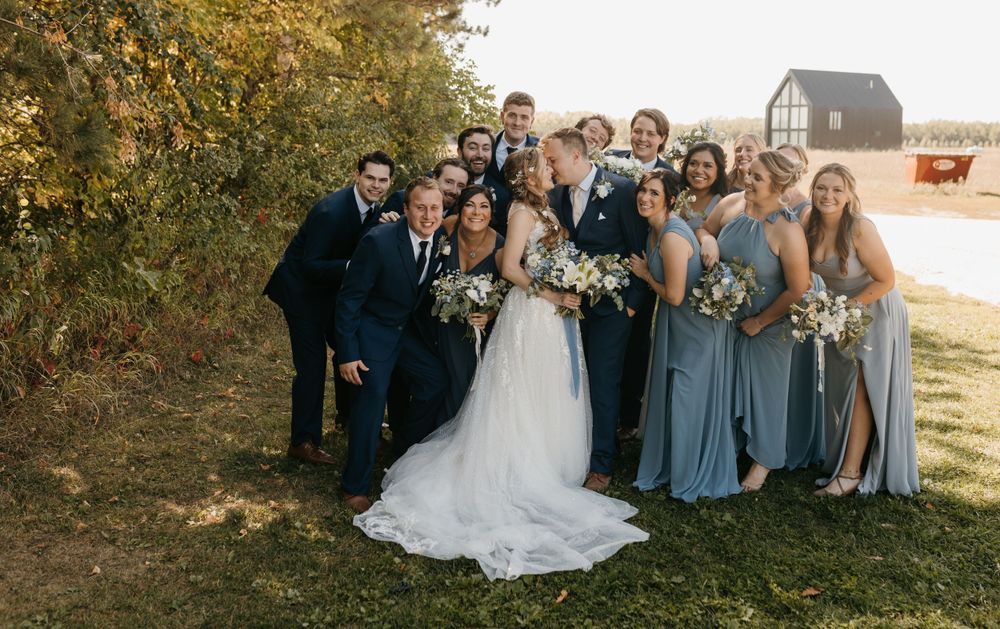 Wedding party laughing together outdoors near a black barn in fall setting.