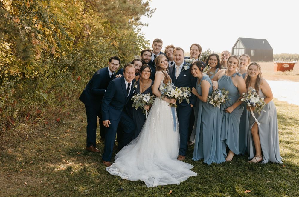 Joyful wedding party candid photo near rustic barn in autumn landscape.