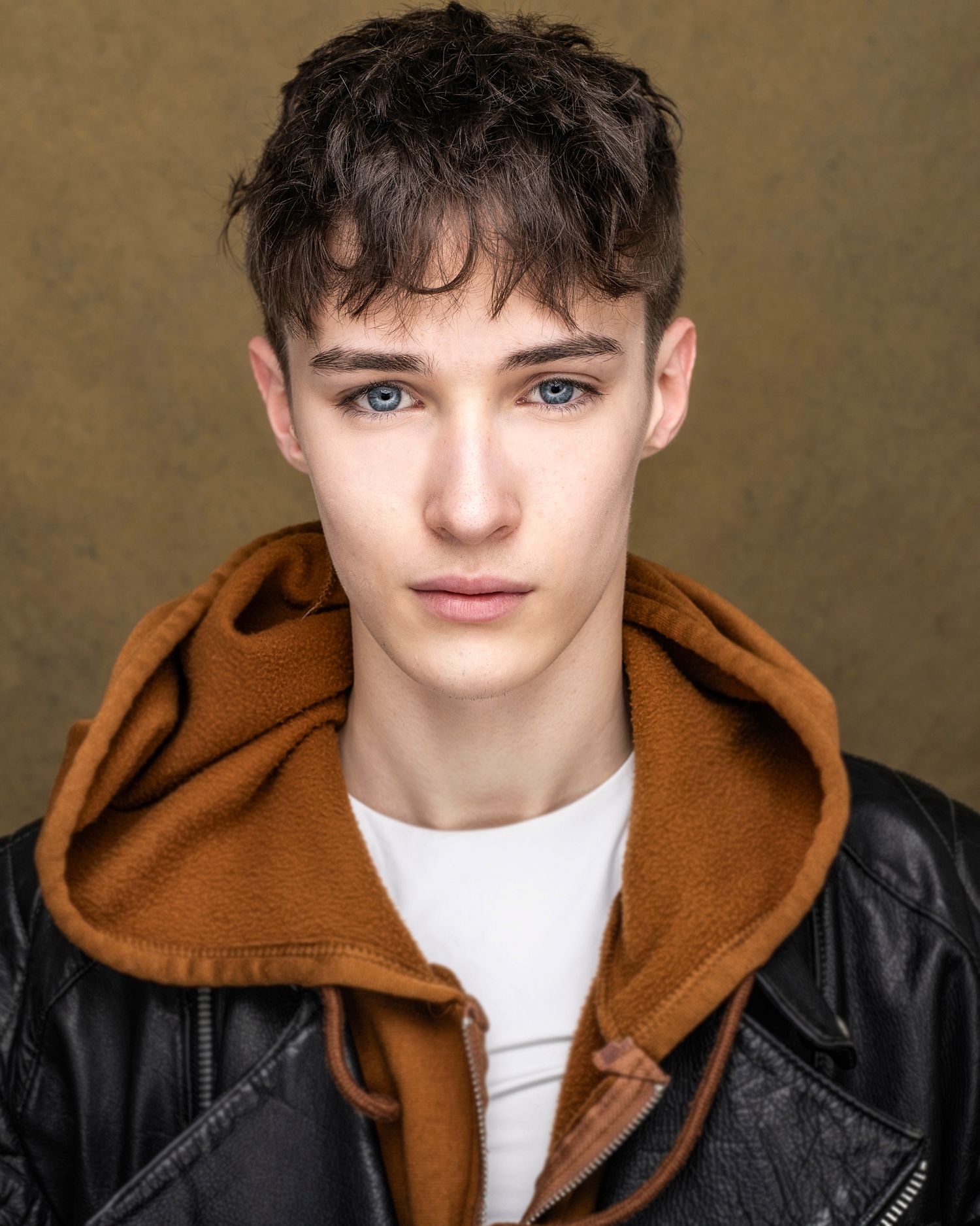 Portrait of person in brown hoodie and leather jacket with striking blue eyes.