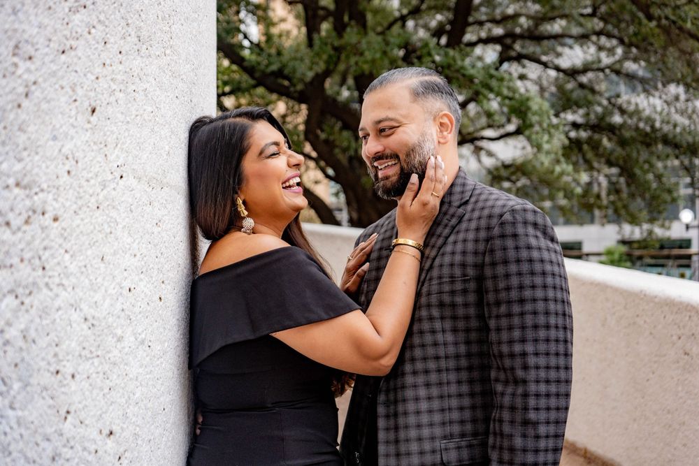 Laughing couple in black and plaid outfits sharing joyful moment against stone column outdoors.