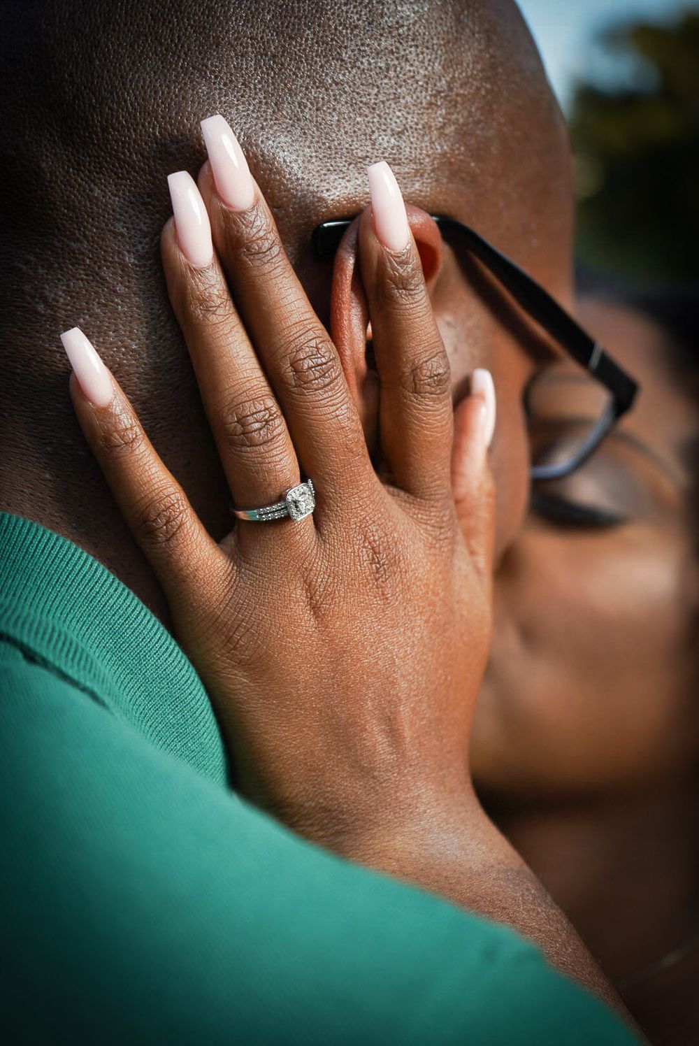 Close-up of woman's hand with long white nails and diamond engagement ring resting on man's chest.