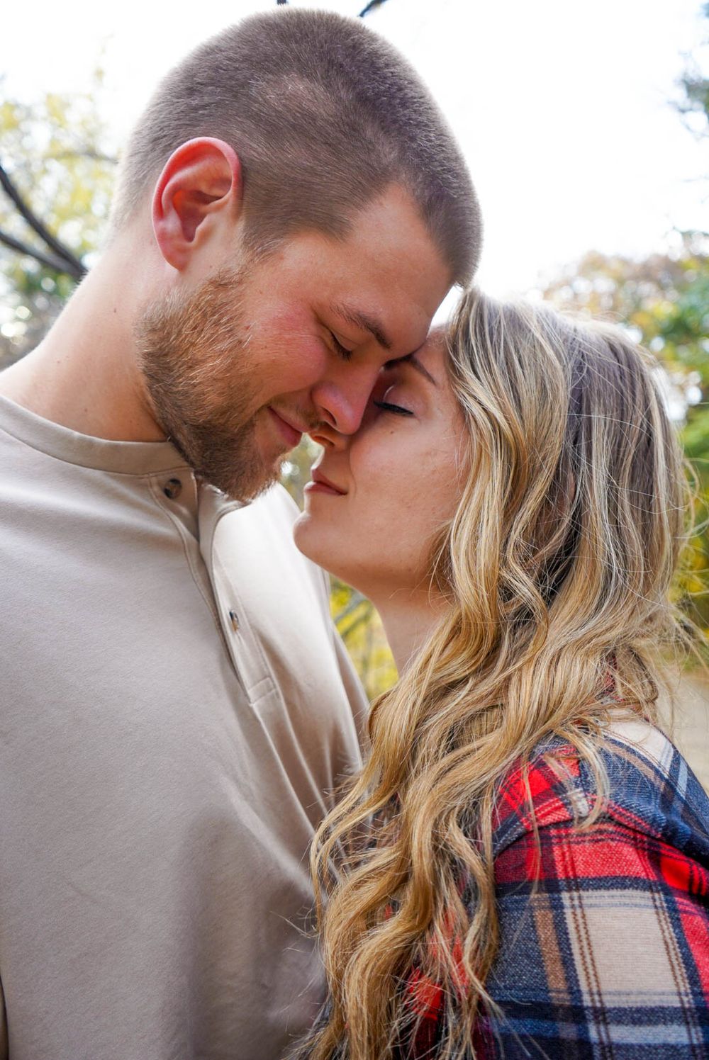 Young couple shares a romantic almost-kiss moment outdoors in casual autumn attire.