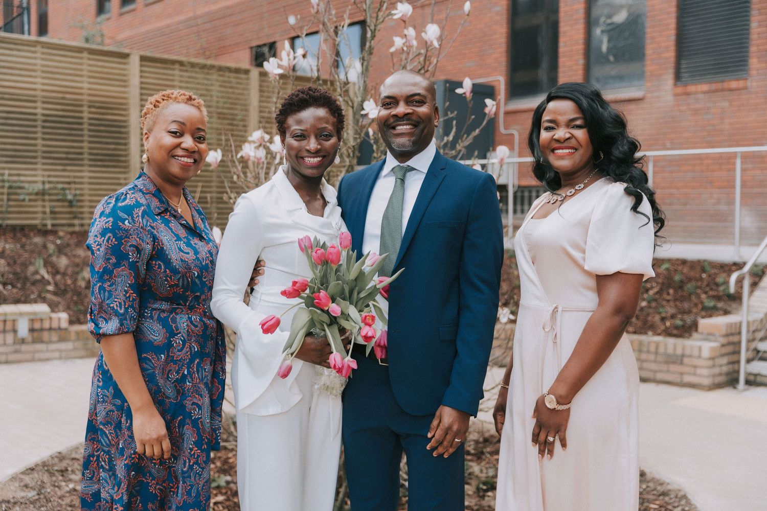 Several people in formal attire stand together for photos outside a brick structure.