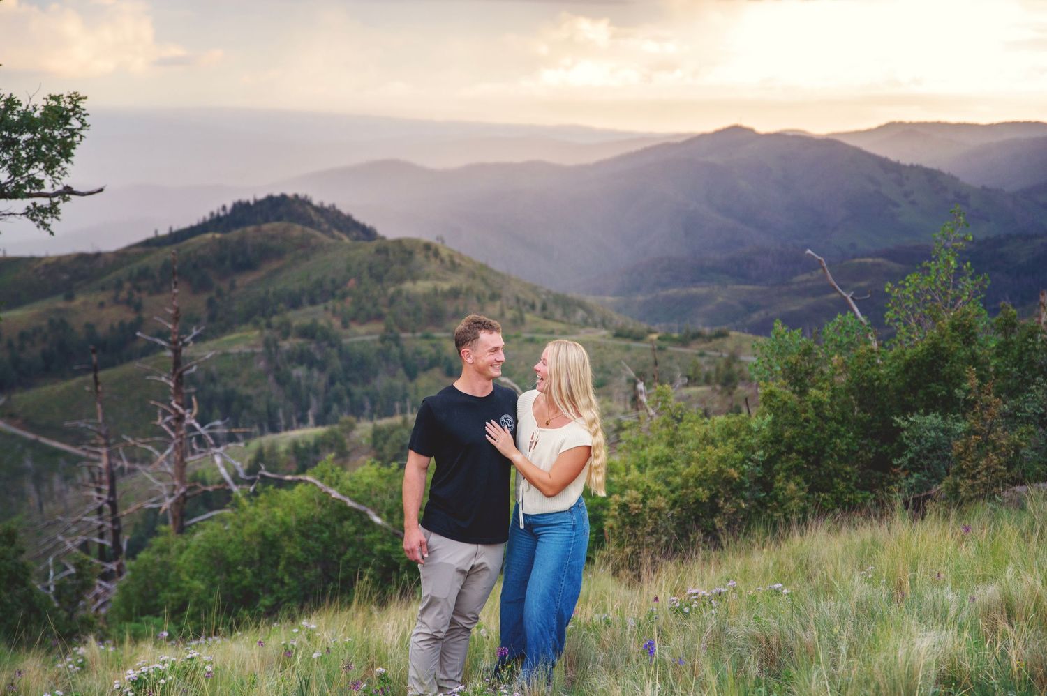 Couple embracing on an overlook with dramatic mountain and cloudy sky views behind them in Ruidoso, NM.
