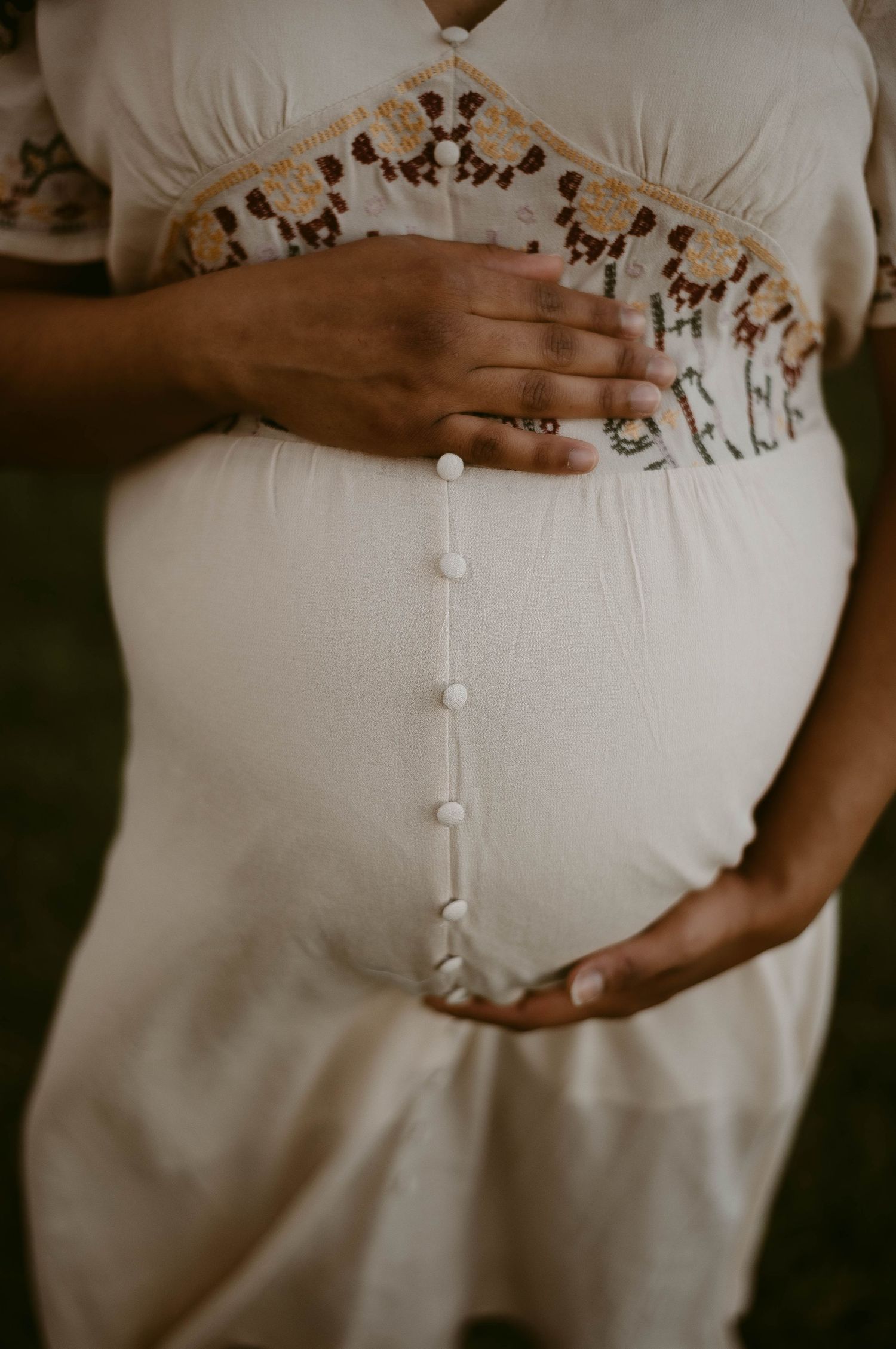 Close-up of embroidered maternity dress details with buttons and delicate lace trim.