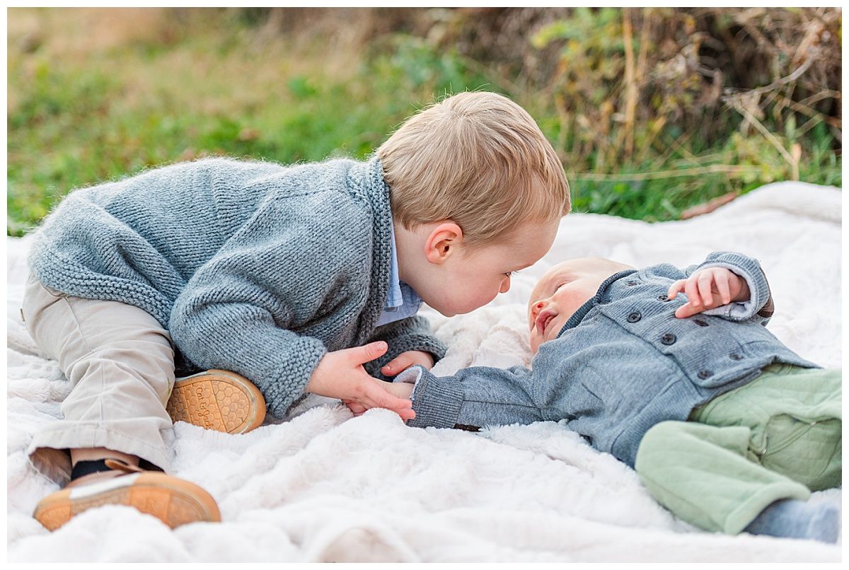 Candid photo of toddler and baby brother holding hands on blanket in park by Jayme Riggleman Photography