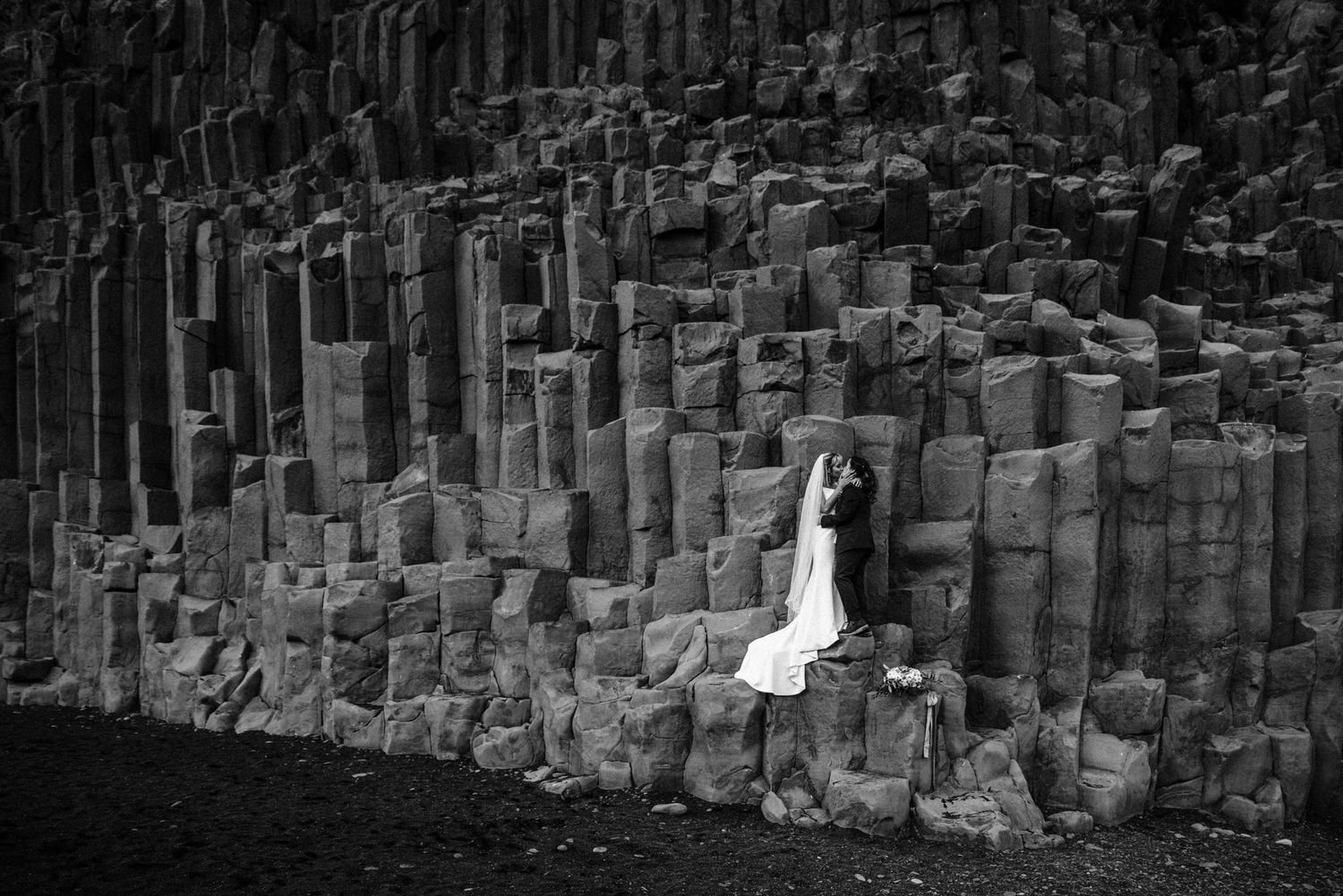 Black and white wedding photo against dramatic basalt column rock formation.