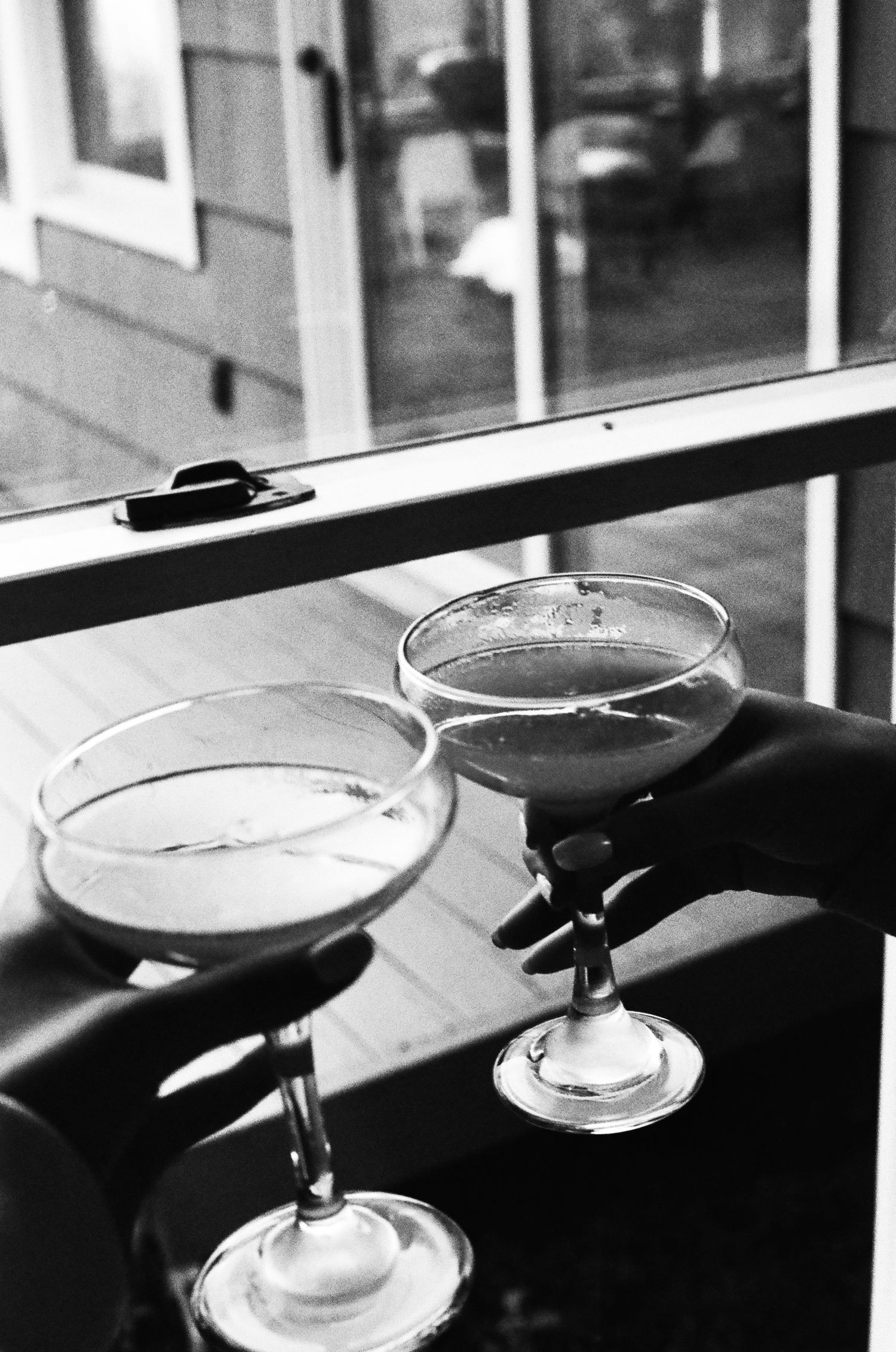Black and white photo of champagne glasses being toasted against a window backdrop.