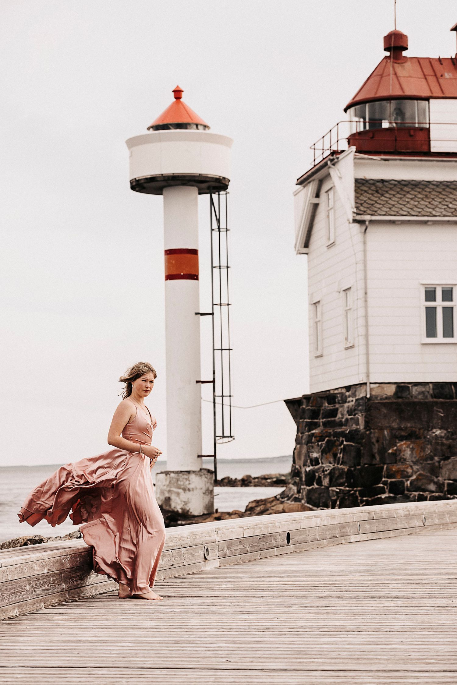 A graceful pose on a wooden pier with a lighthouse and white building in the background.