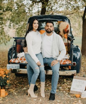Couple sitting on tailgate of vintage blue truck surrounded by pumpkins and fall decor.