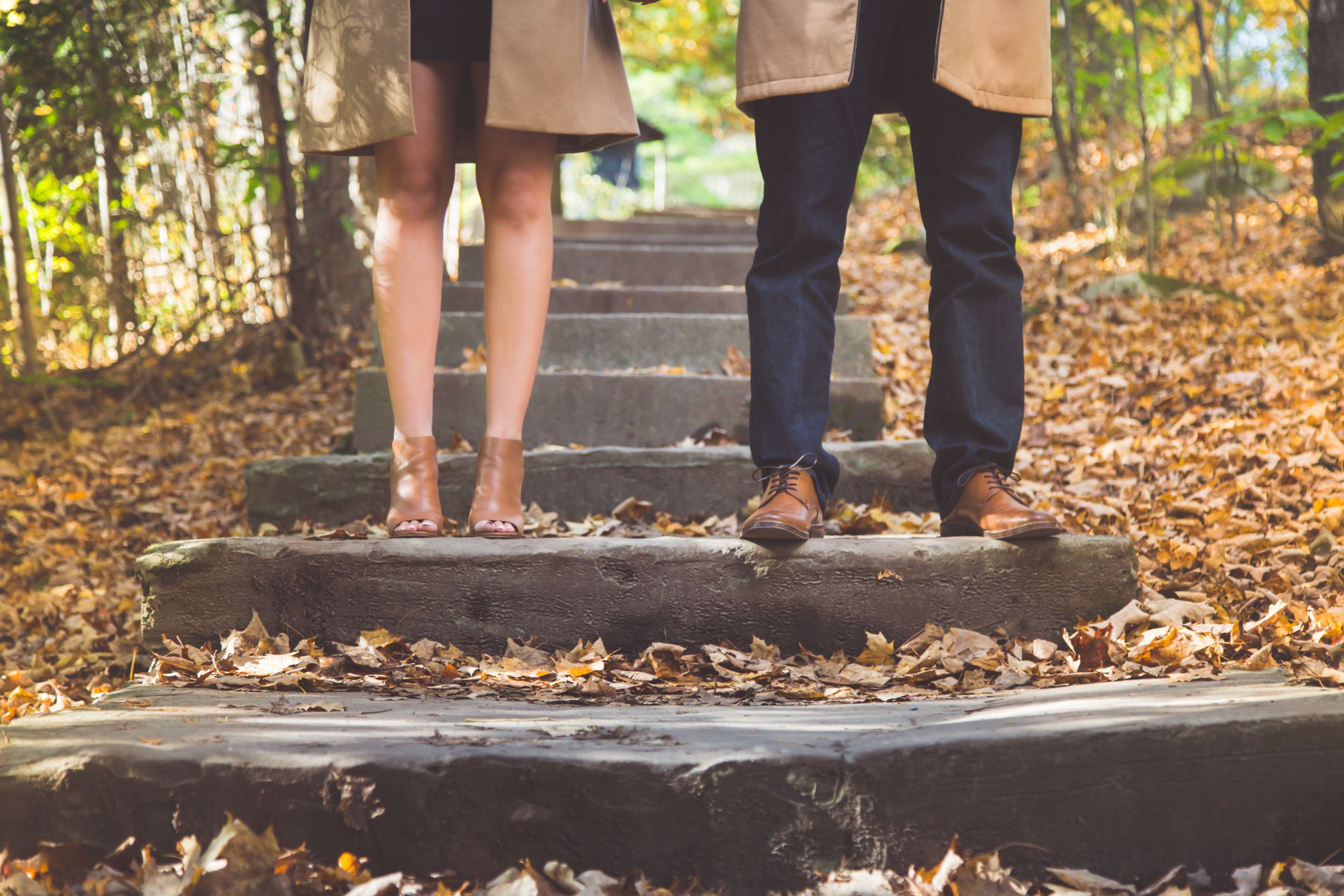 Close-up of feet standing on wooden steps covered in fallen autumn leaves.
