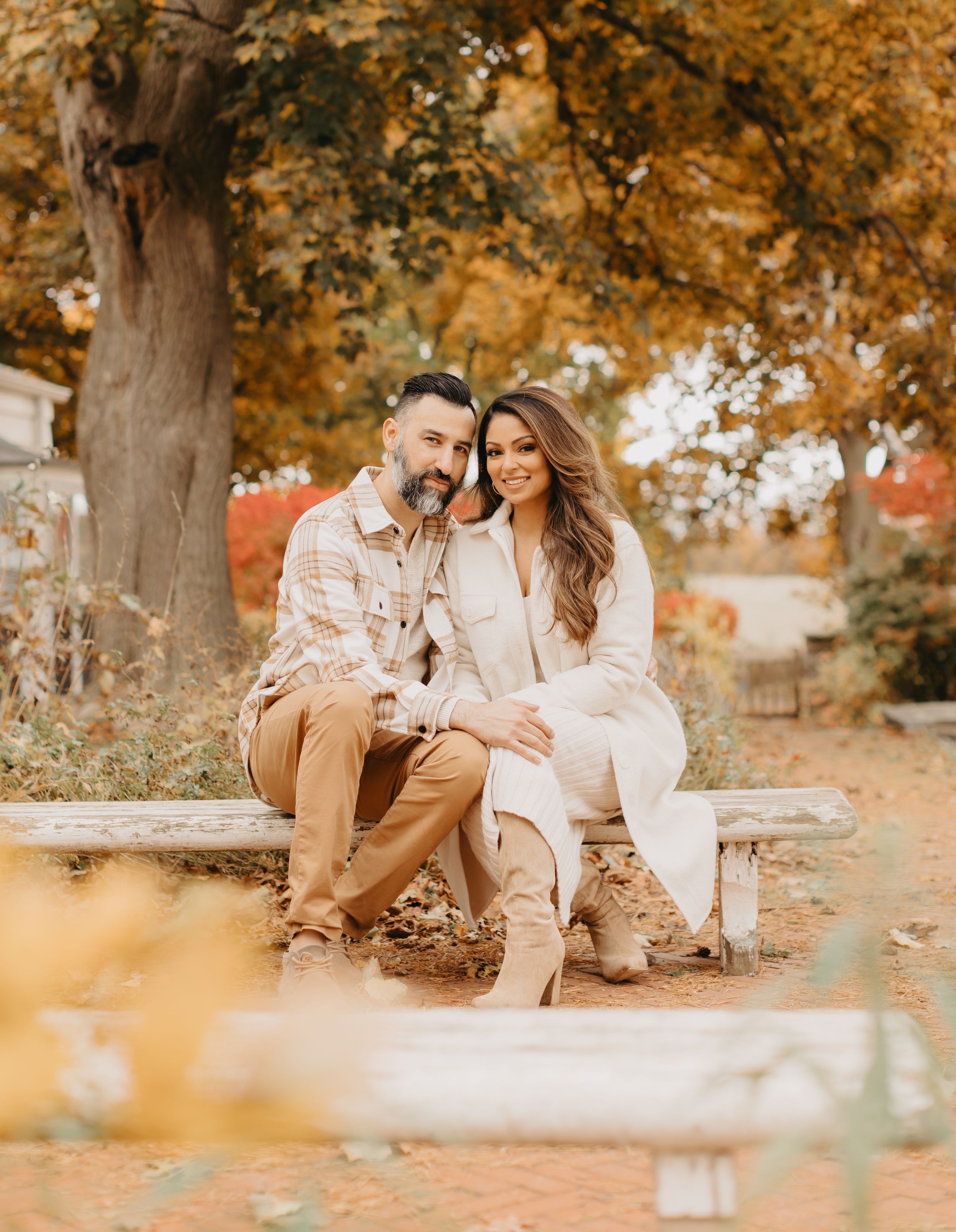 Family in white outfits sitting together under golden autumn trees.