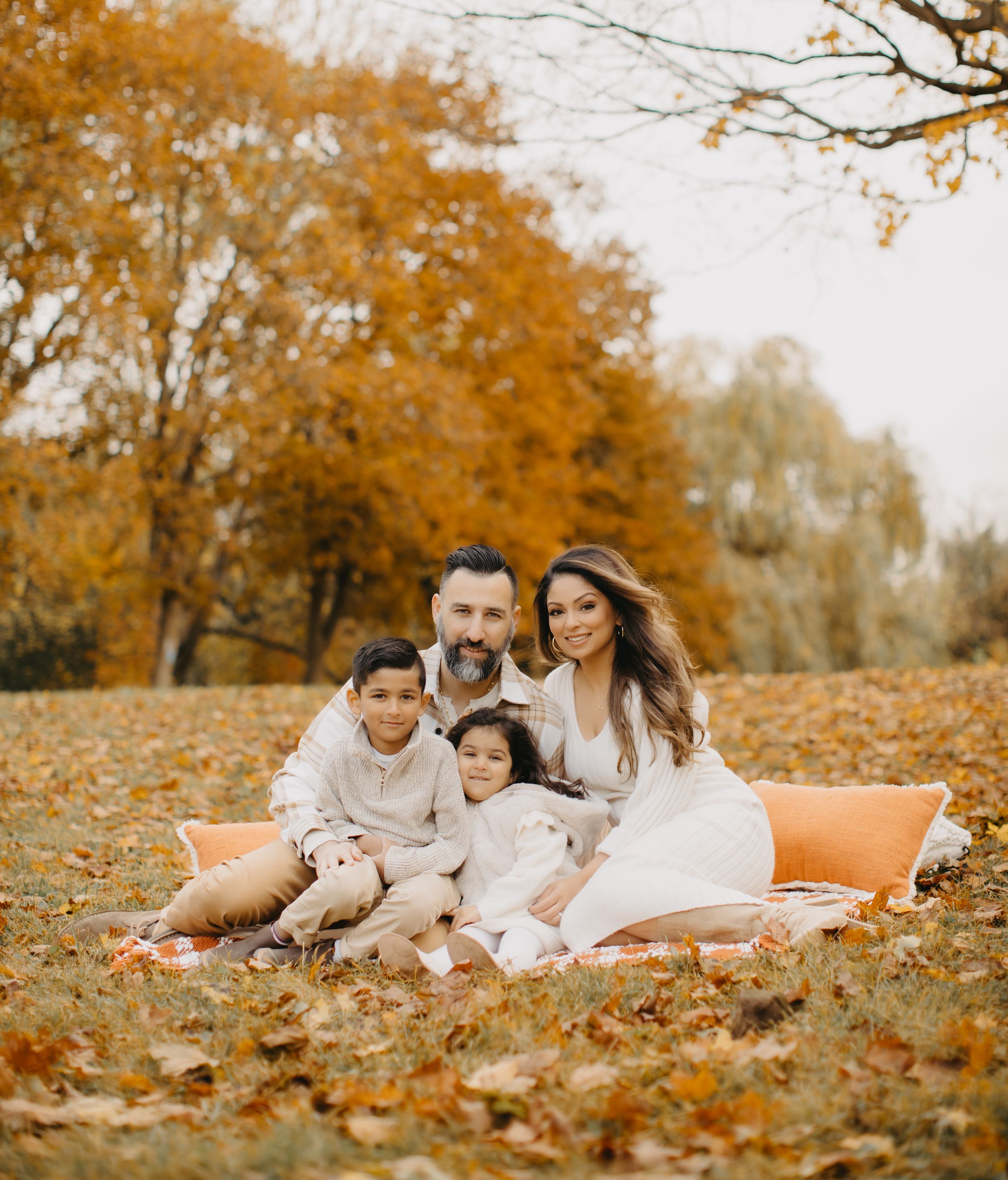 Family lying on orange blanket surrounded by golden autumn leaves.