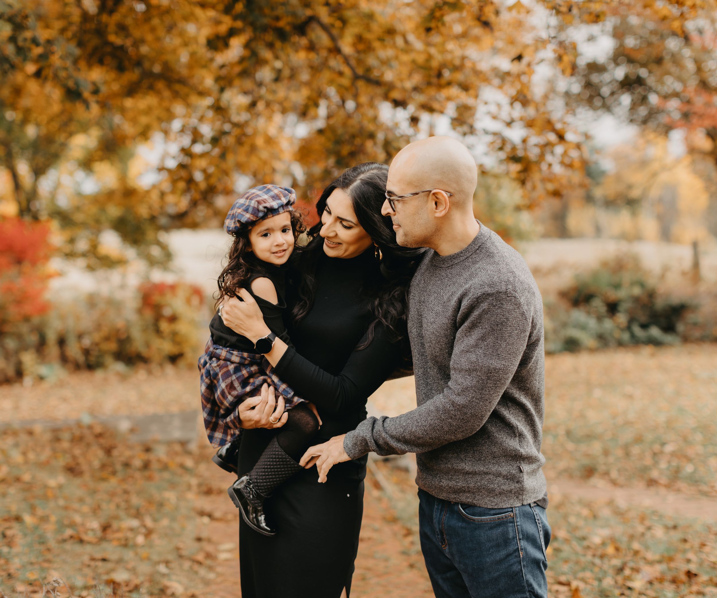 Family portrait session in a park during golden autumn season with fallen leaves.