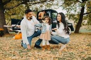 Family sitting together on fallen leaves near a vintage truck during autumn.