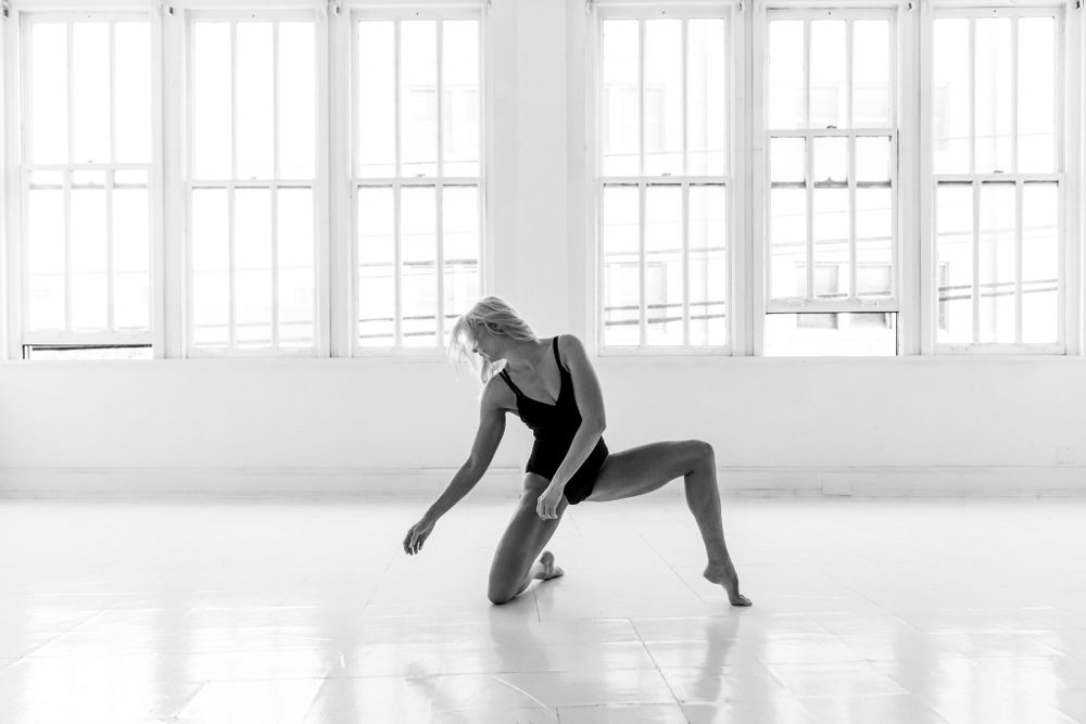 Modern dancer in athletic wear performing contemporary movement in bright studio space.