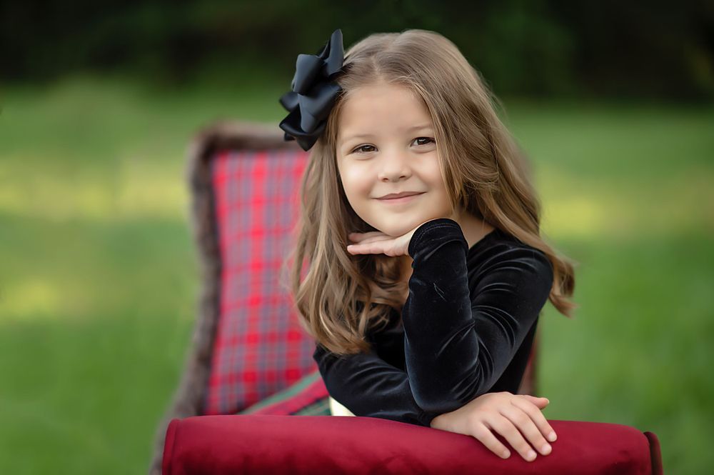 Holiday portrait session featuring cozy winter outfits and plaid decor on maroon furniture.