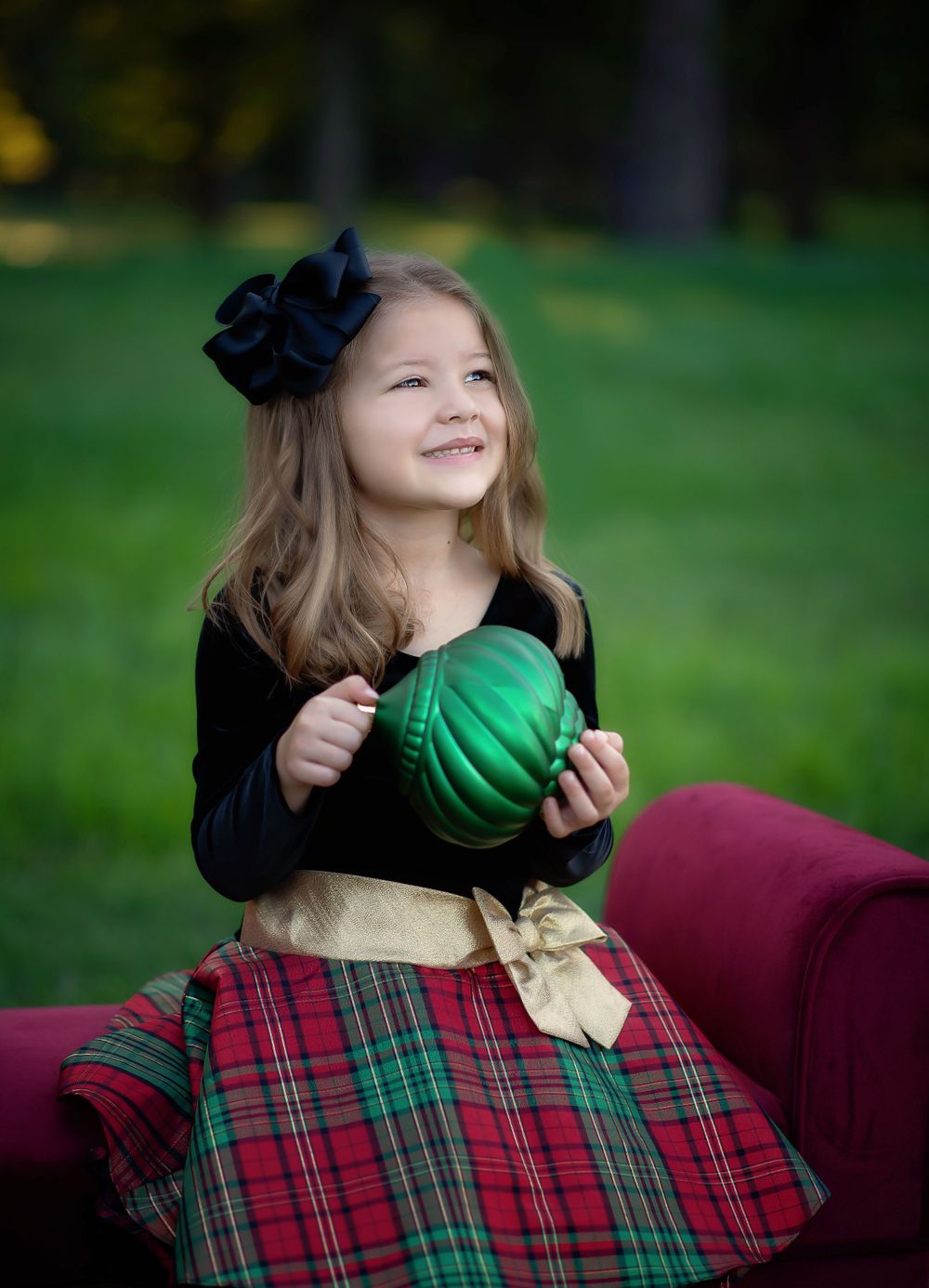 Seasonal portrait setup with red plaid blanket and black velvet clothing against green outdoor backdrop.