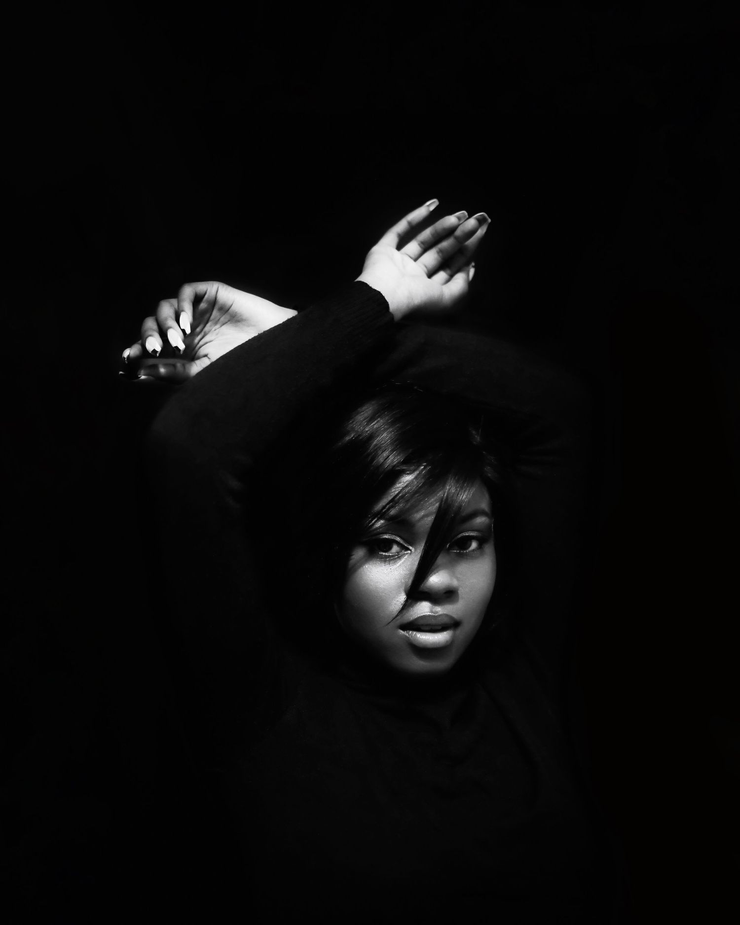 Dramatic black and white studio portrait with raised hands casting shadows against dark background.