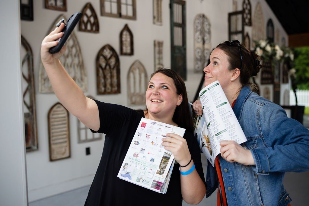 Two people taking a cheerful selfie while holding documents in an indoor venue.