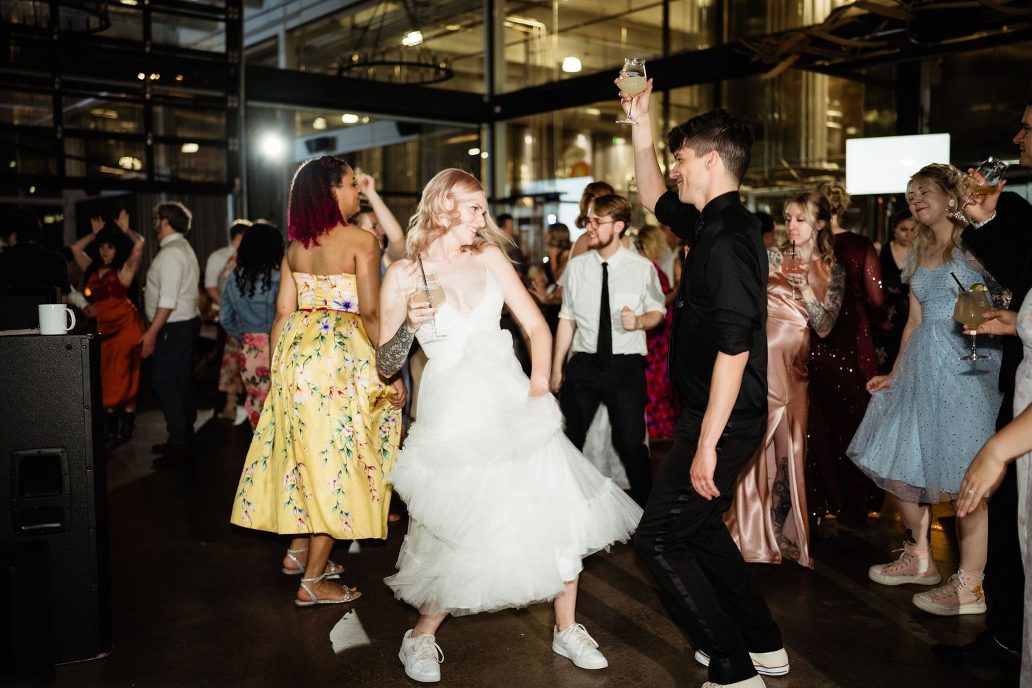 Wedding guests dancing on a dark dance floor with the bride in a white dress and sneakers.