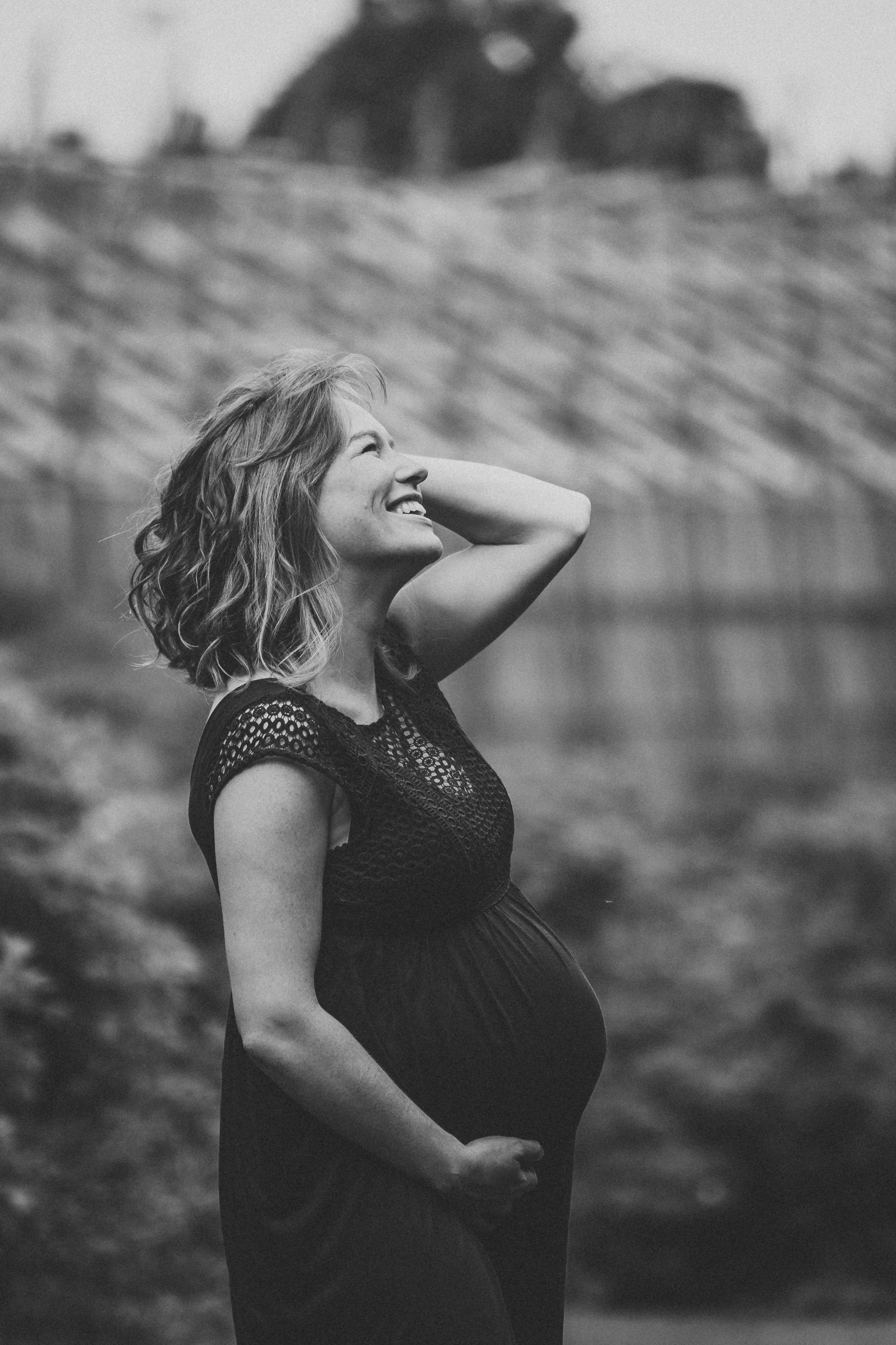 A black and white portrait of an expectant mother laughing outdoors.