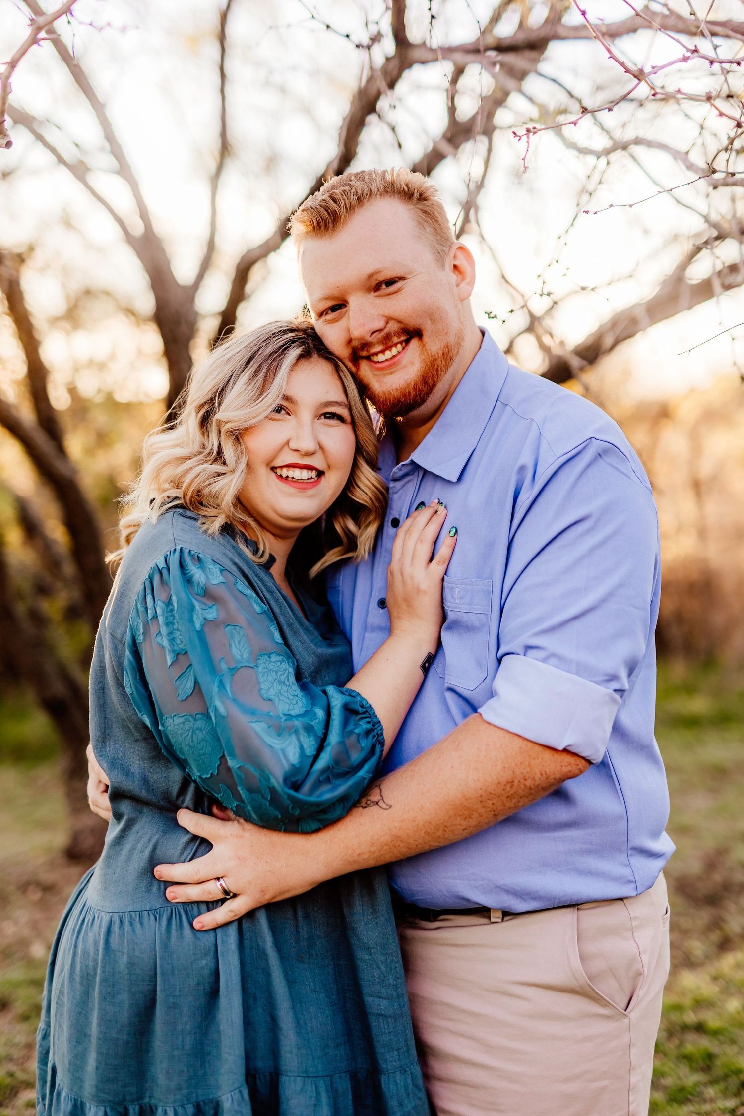 Couple in blue outfits embrace during outdoor sunset photo session.