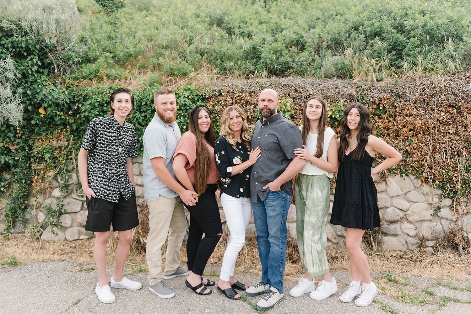 A group of people pose together against a stone wall outdoors in casual summer attire.