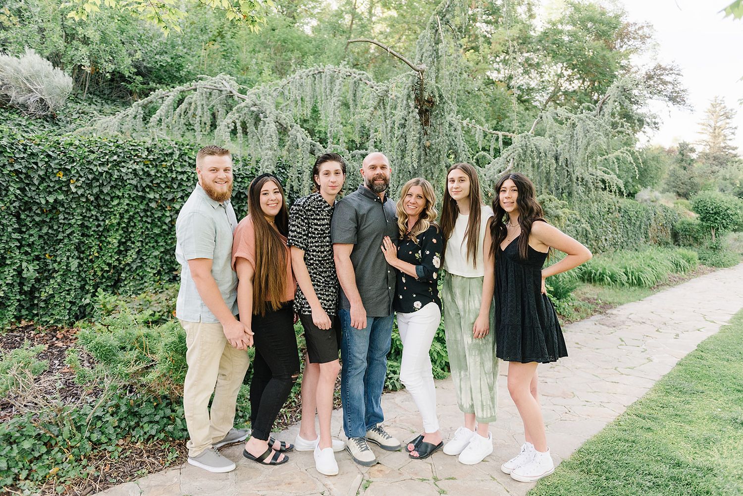 A group portrait of people standing together in coordinated outfits against a green garden backdrop.