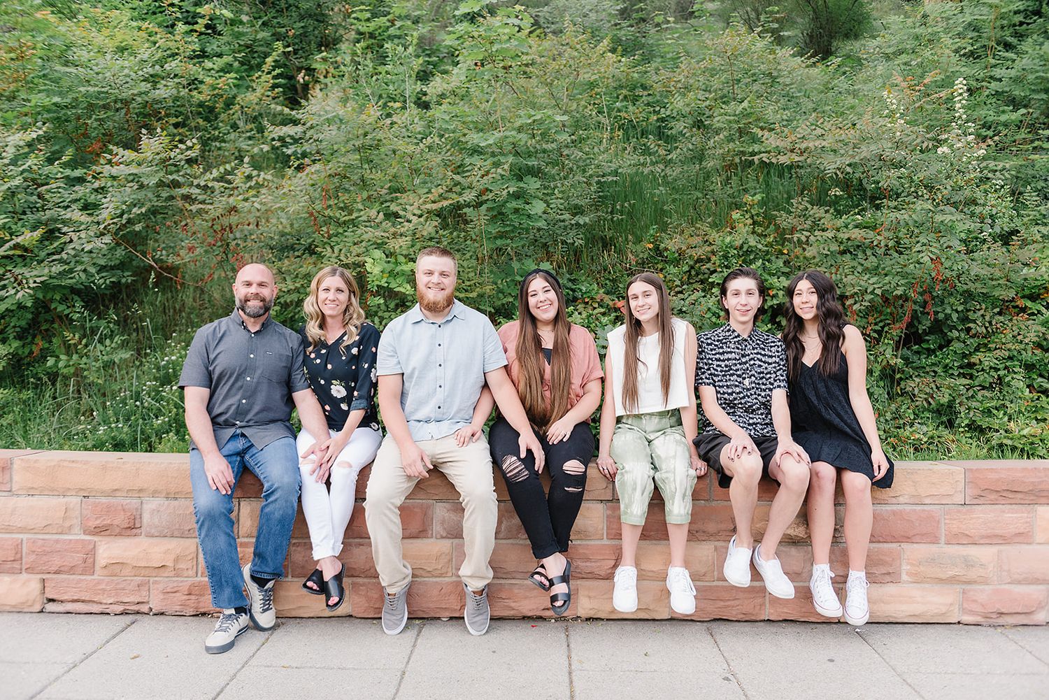 A casual group photo of people sitting on a brick wall surrounded by lush greenery.
