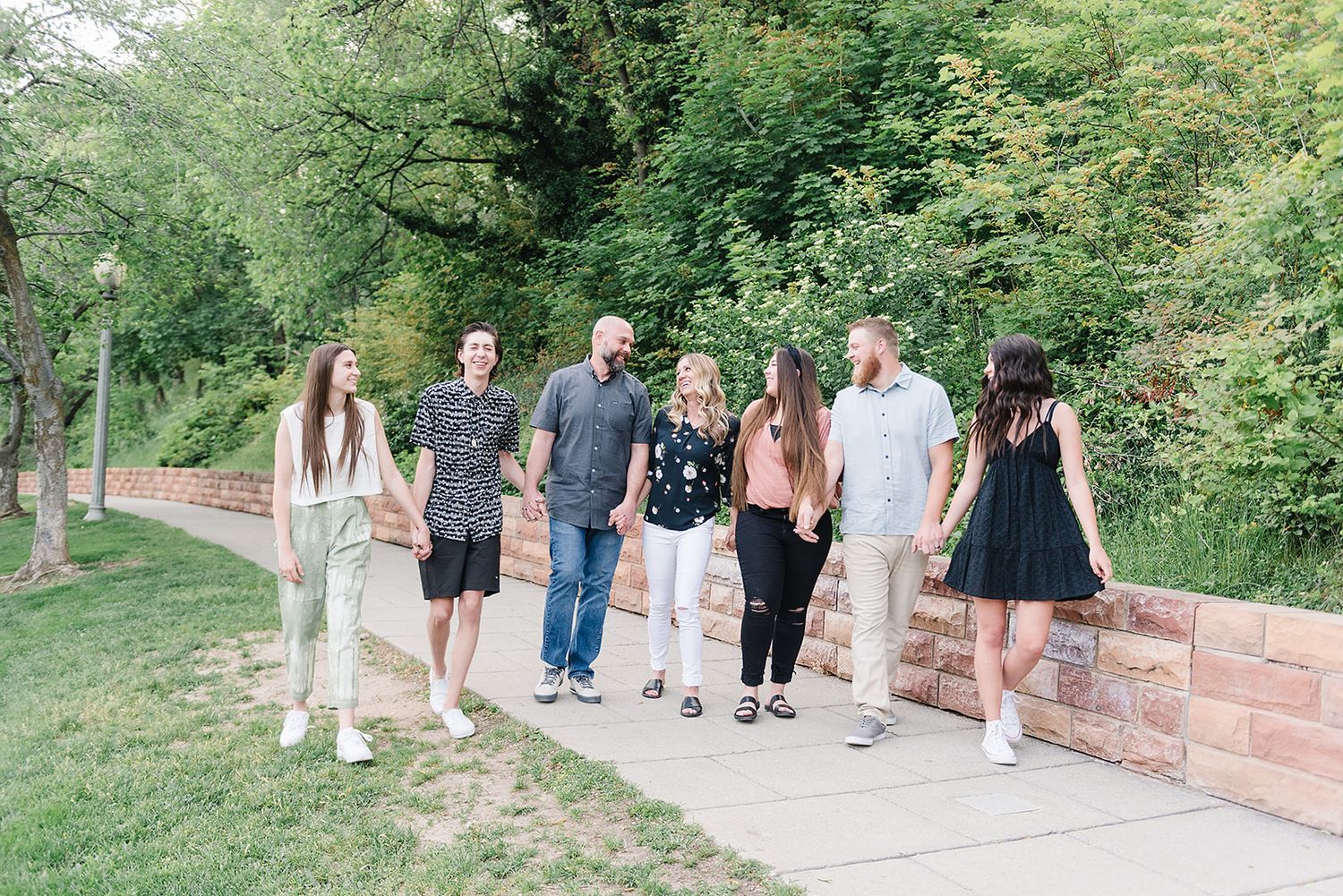 A group of friends in casual attire standing and posing along a brick wall in a garden setting.