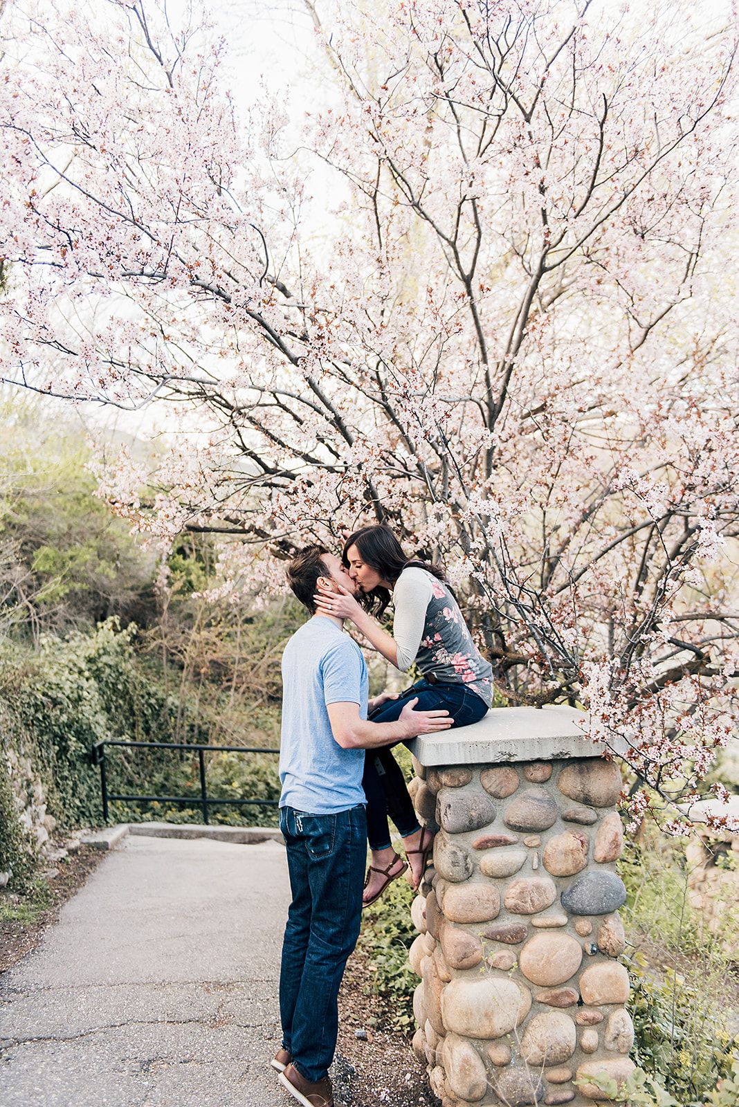 Romantic moment captured under blooming spring cherry blossoms by stone pillar.
