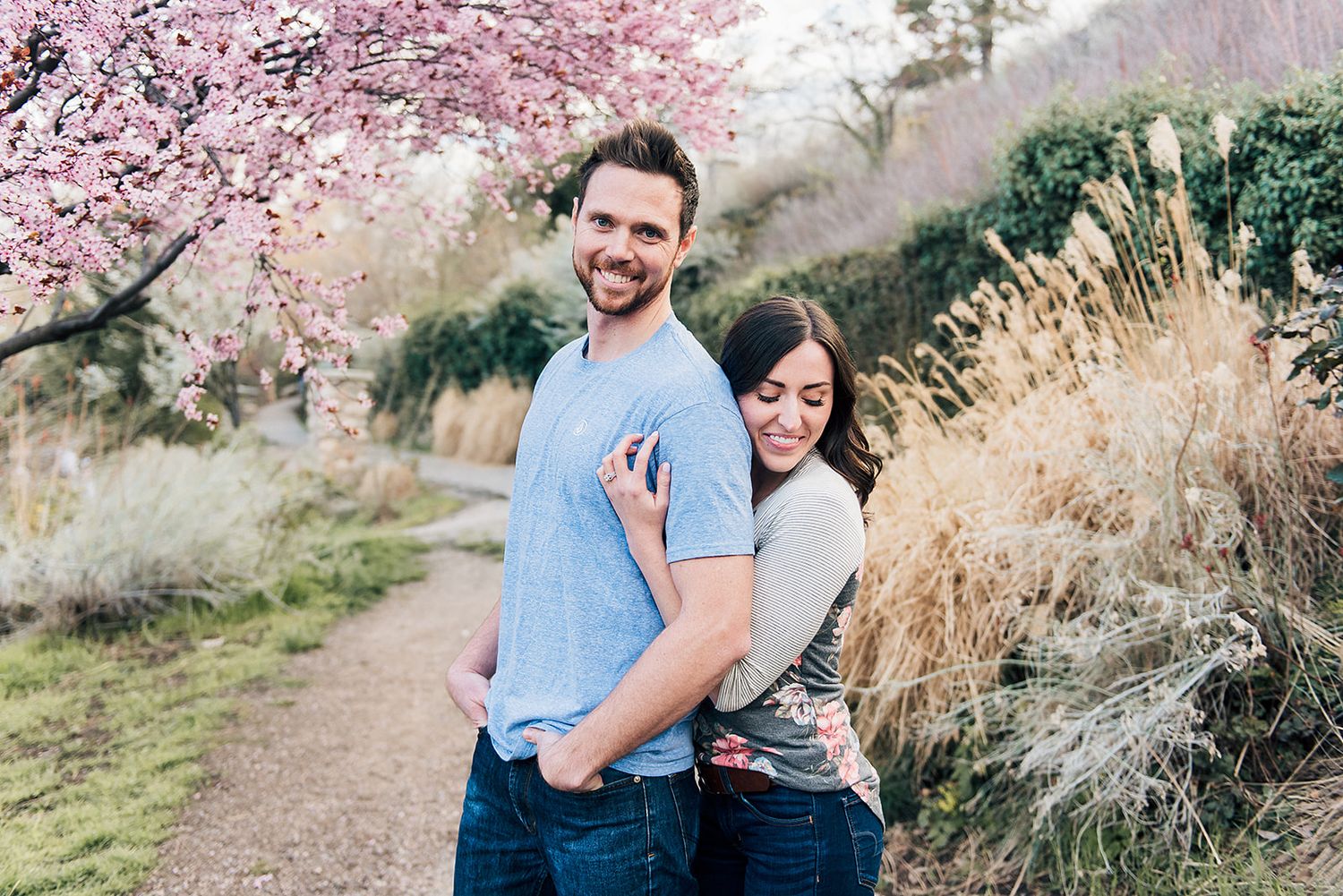 Couple sharing romantic moment beneath blooming cherry blossom trees on nature trail.