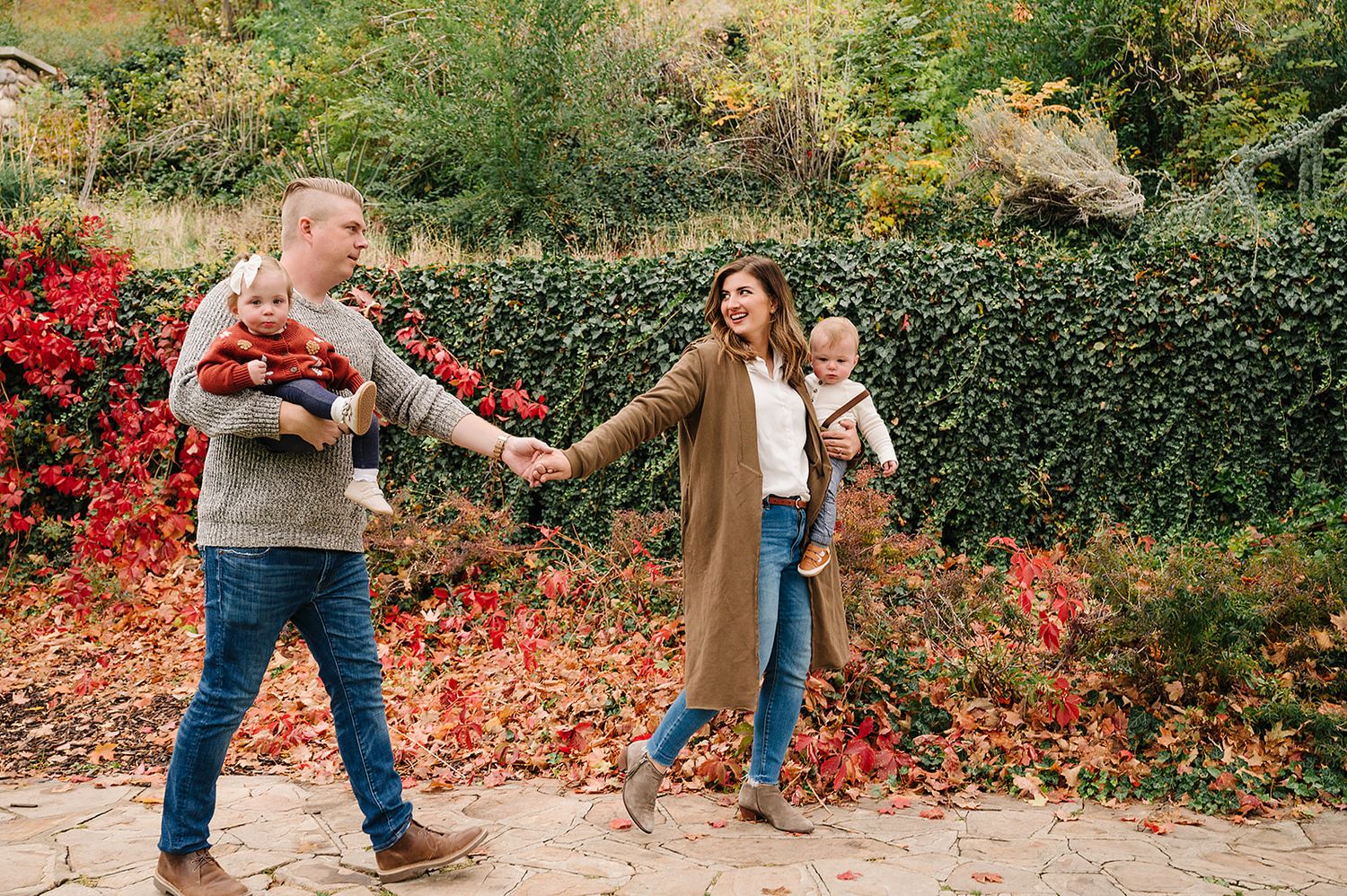 A playful family moment captured in front of vibrant red autumn foliage.