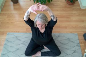 Person performing stretching exercise on geometric patterned mat in sunlit room.