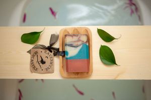 Artistic flatlay with wooden clock and soap bar styled with green leaves.