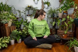 Person in green sweatshirt surrounded by houseplants in living space.
