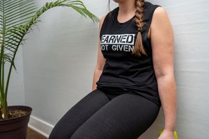 Athletic woman in black tank top sitting next to tropical plant.