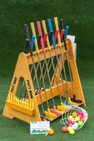 Colorful mini golf putters arranged in wooden stand with balls and scorecard.
