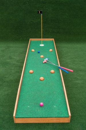 Miniature golf putting green with scattered balls and blue putter on wooden frame.