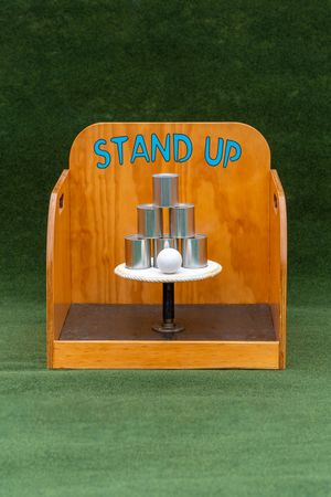 Classic carnival game 'Stand Up' with metal cans and white ball displayed on wooden platform.
