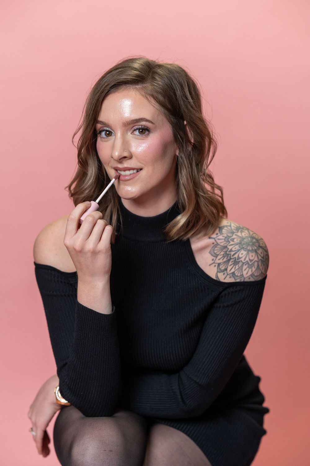 A woman in a black sweater poses against a pink background.