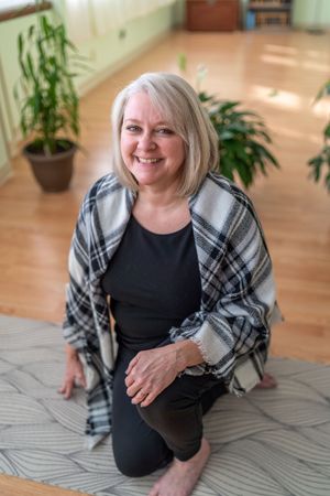 Person sitting on yoga mat wearing plaid wrap in sunny indoor setting.